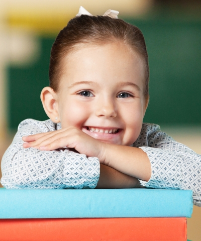 Uśmiechnięta dziewczynka oparta na kolorowych książkach – LabStar Kids